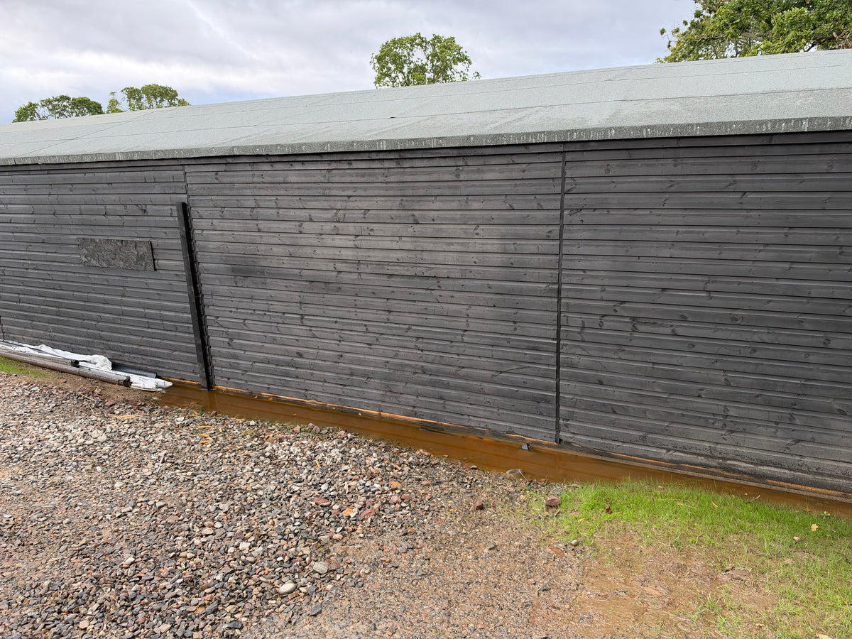 Rainwater pooled against the dark timber wall of the stable, over the gravel edge