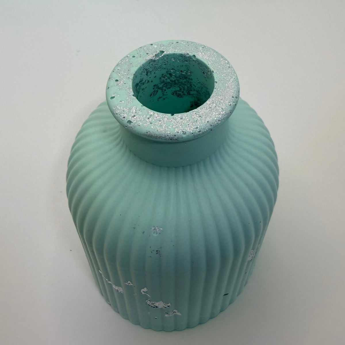 A small ribbed ceramic vase in a light aqua or mint green color with distressed white paint details, shown on a plain white background.