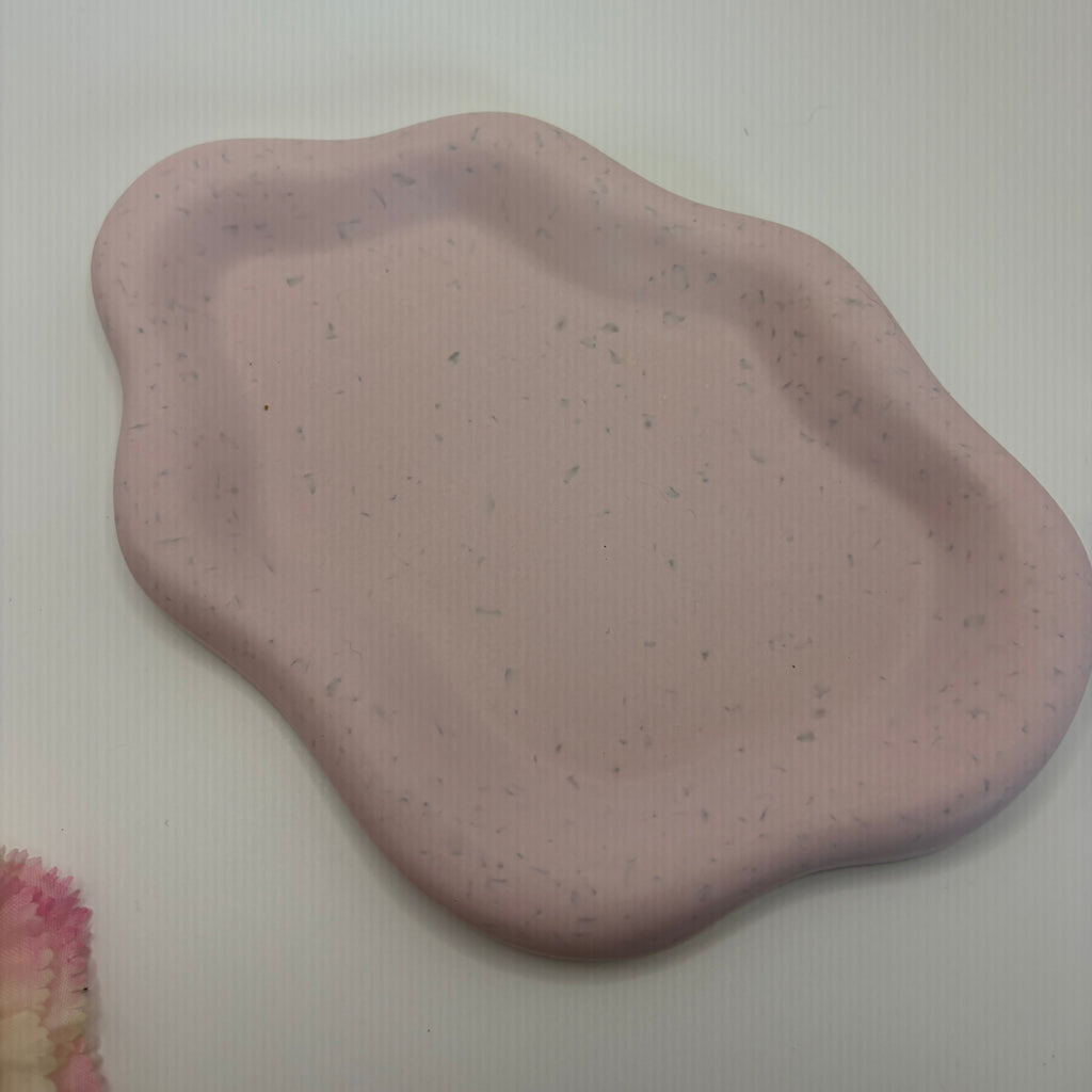 A small, irregularly shaped pink tray with a speckled texture, photographed on a plain white surface.