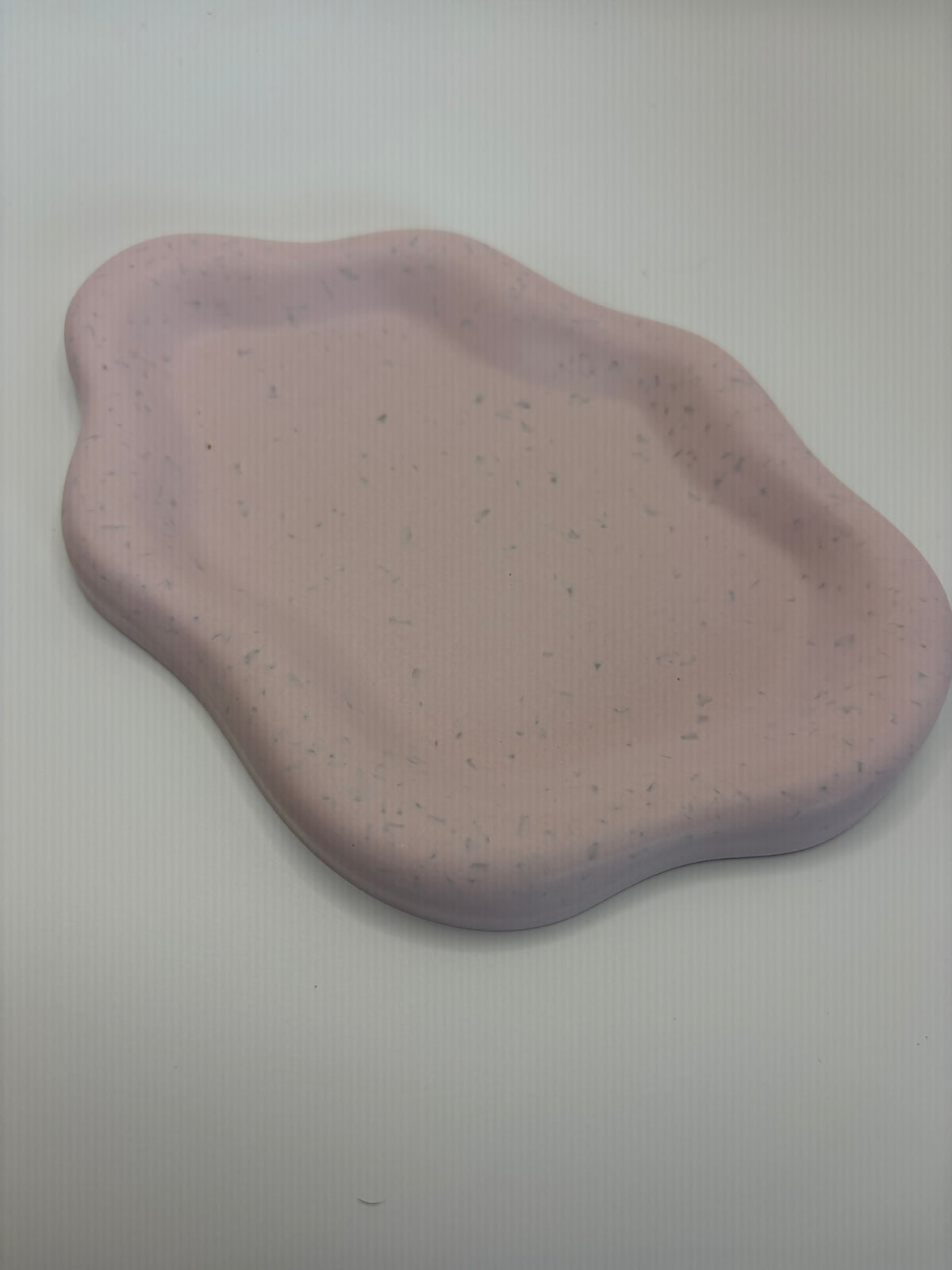 An organic-shaped, wavy ceramic dish in a dusty pink color with subtle gray and white speckles, shown on a plain light gray background.