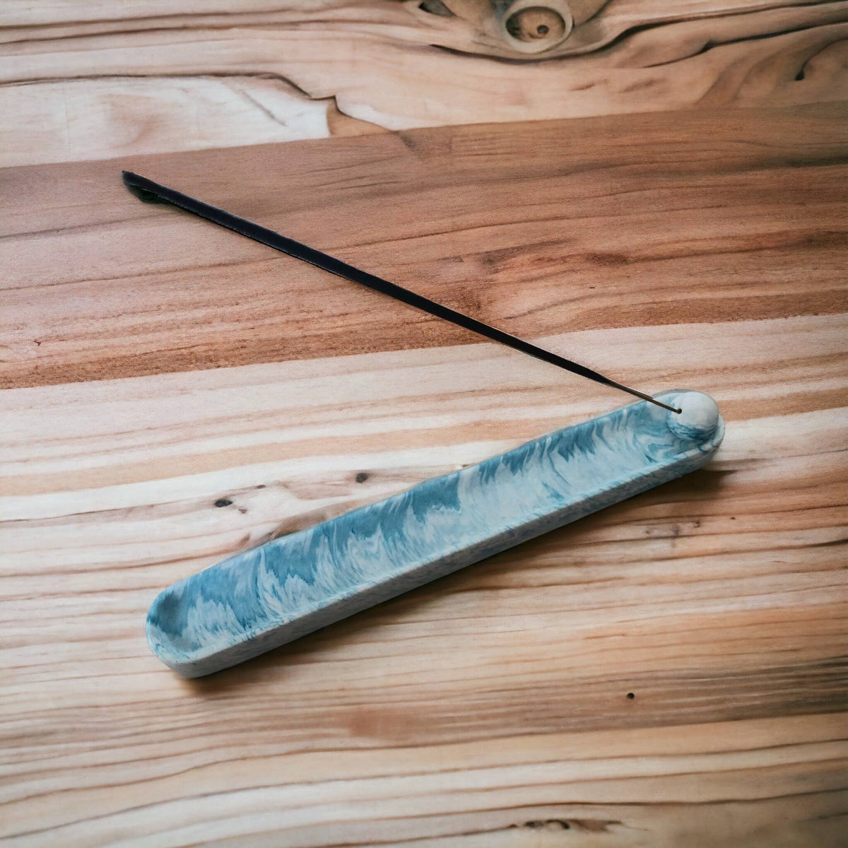 Blue marble Jesmonite incense holder with incense stick resting at an angle, overhead view on a wooden surface, Croft & Cleo