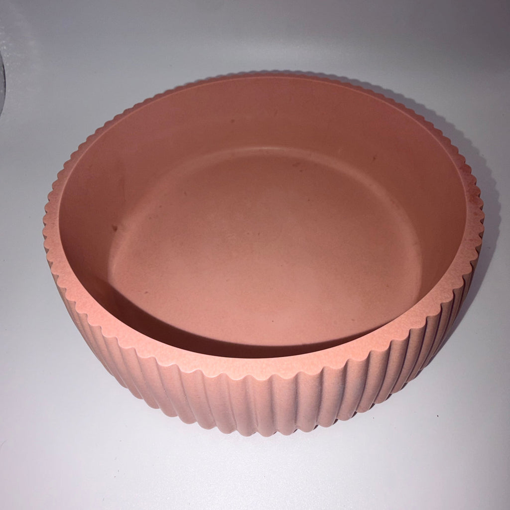 A terracotta-colored round planter pot with a fluted, ribbed exterior and a smooth, slightly tapered interior, shown on a plain light gray background.