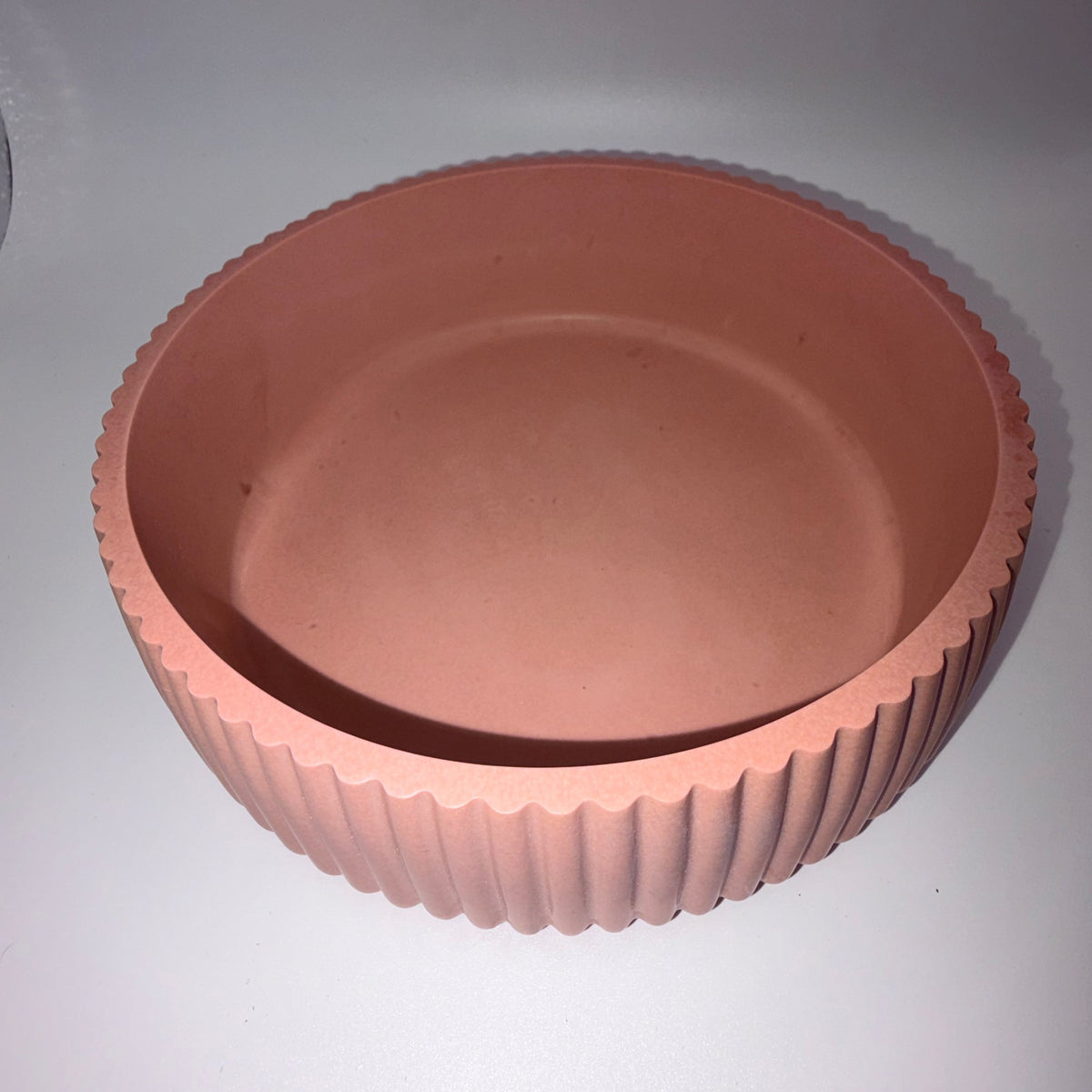 A terracotta-colored round planter pot with a fluted, ribbed exterior and a smooth, slightly tapered interior, shown on a plain light gray background.