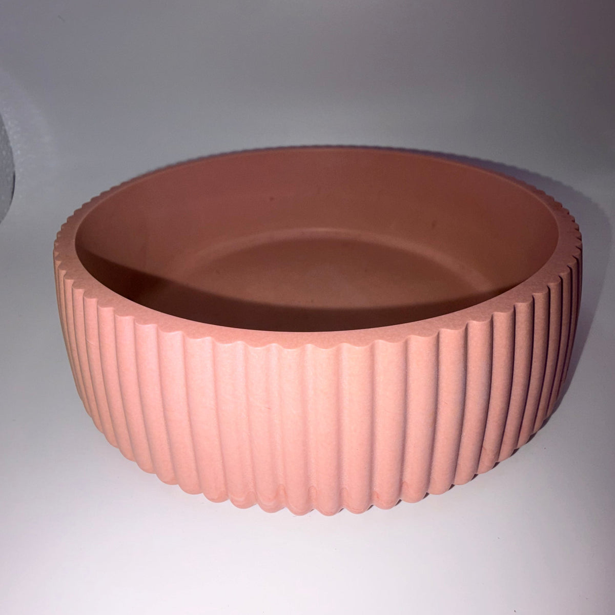 A terracotta-colored round planter with a fluted, ribbed exterior and a smooth, slightly tapered interior, shown on a neutral gray background.