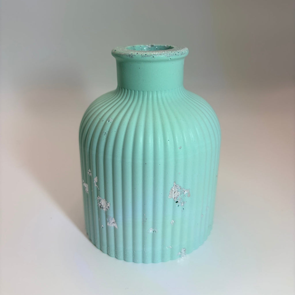 A small ribbed ceramic vase in a light mint green or aqua color with distressed white speckles, shown on a plain light background.