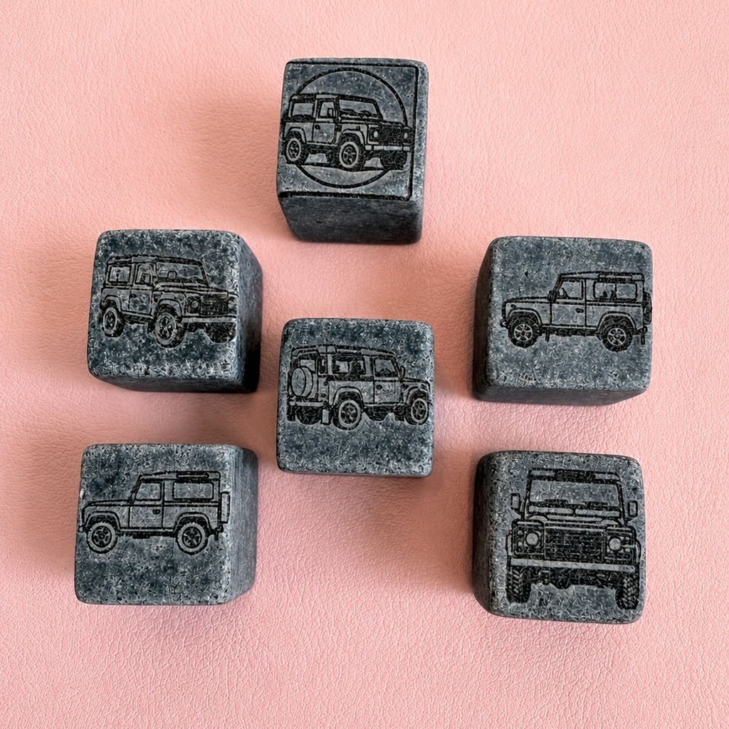 Six dark gray stone cubes engraved with different vehicle illustrations, arranged on a soft pink textured background.