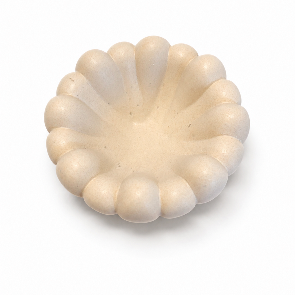 A small scalloped ceramic dish or candle holder in a warm cream or off-white color, photographed from a top-down perspective on a clean white background.