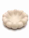 A small, scalloped ceramic dish in a warm cream or off-white color, photographed on a seamless white background.