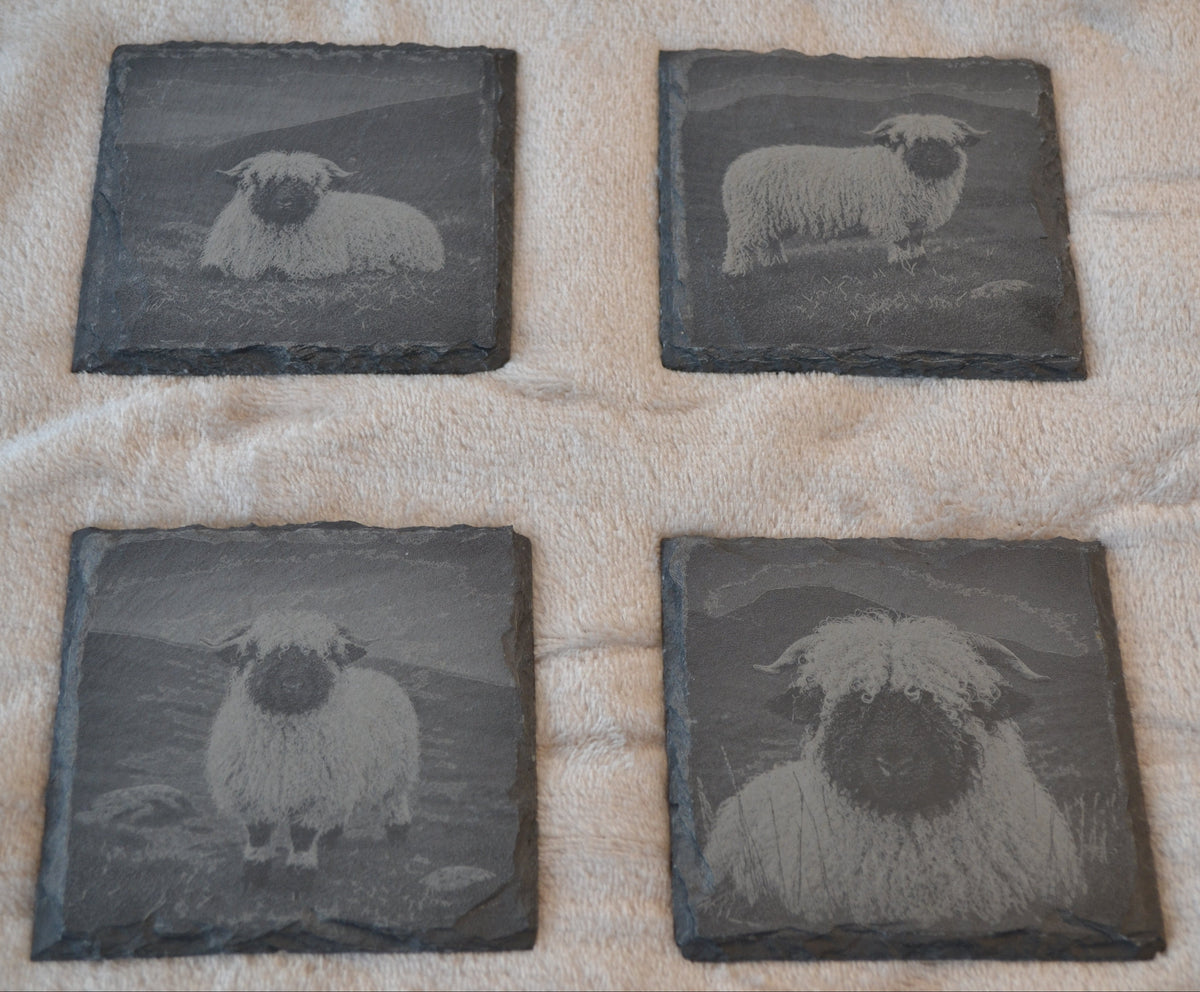 Four square slate coasters featuring engraved images of different sheep, arranged in a 2x2 grid on a textured cream-colored blanket.