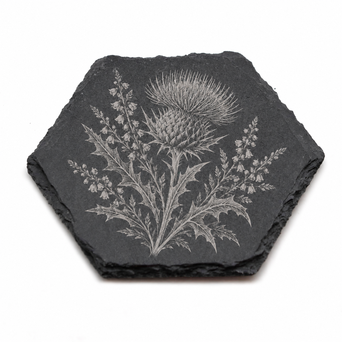 A hexagonal dark gray slate coaster featuring a detailed engraved botanical design of a thistle and surrounding leaves, shown on a plain white background.